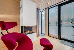 Ein modernes Interieur mit Kamin, roten Sesseln und einer großen Glastür zum Außenbereich.