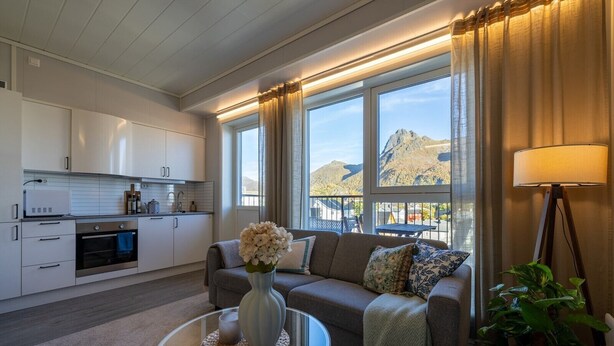 A modern kitchen with white cabinets, a built-in oven, and a dining area with a table and chairs. - Aurora View Apartment Svolvær (Vågan)