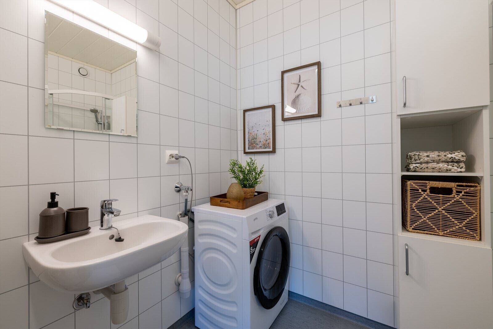 A bathroom with a sink, mirror, washing machine, and storage shelves.