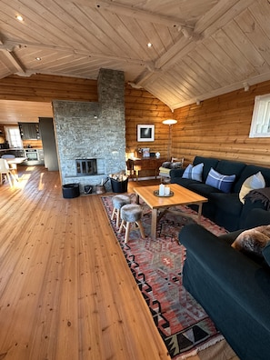 Ein rustikales Blockhaus-Interieur mit Kamin aus Stein, Holzböden, einer Couch und einem Essbereich.