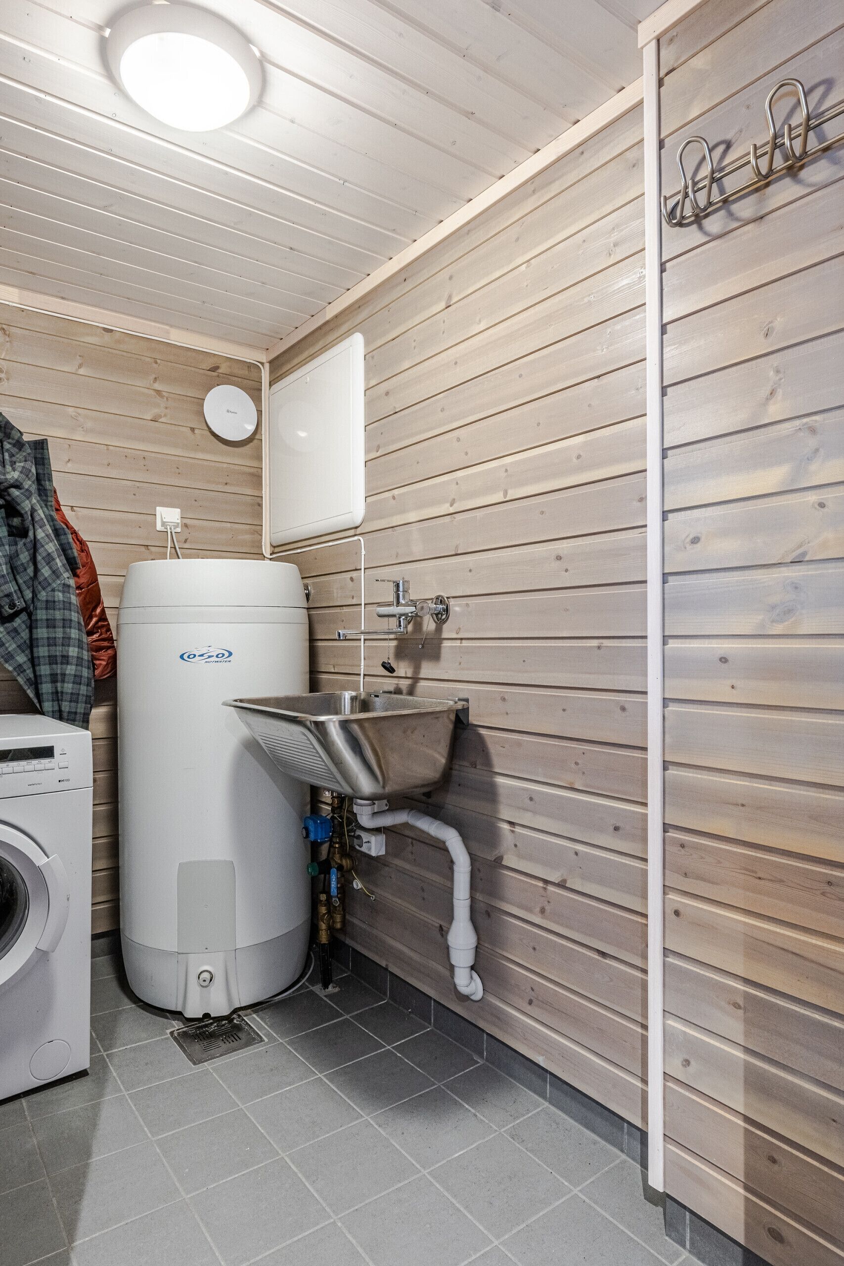 Une petite salle de bain équipée d’un lave-linge, d’un chauffe-eau et d’un évier avec un bac en métal.