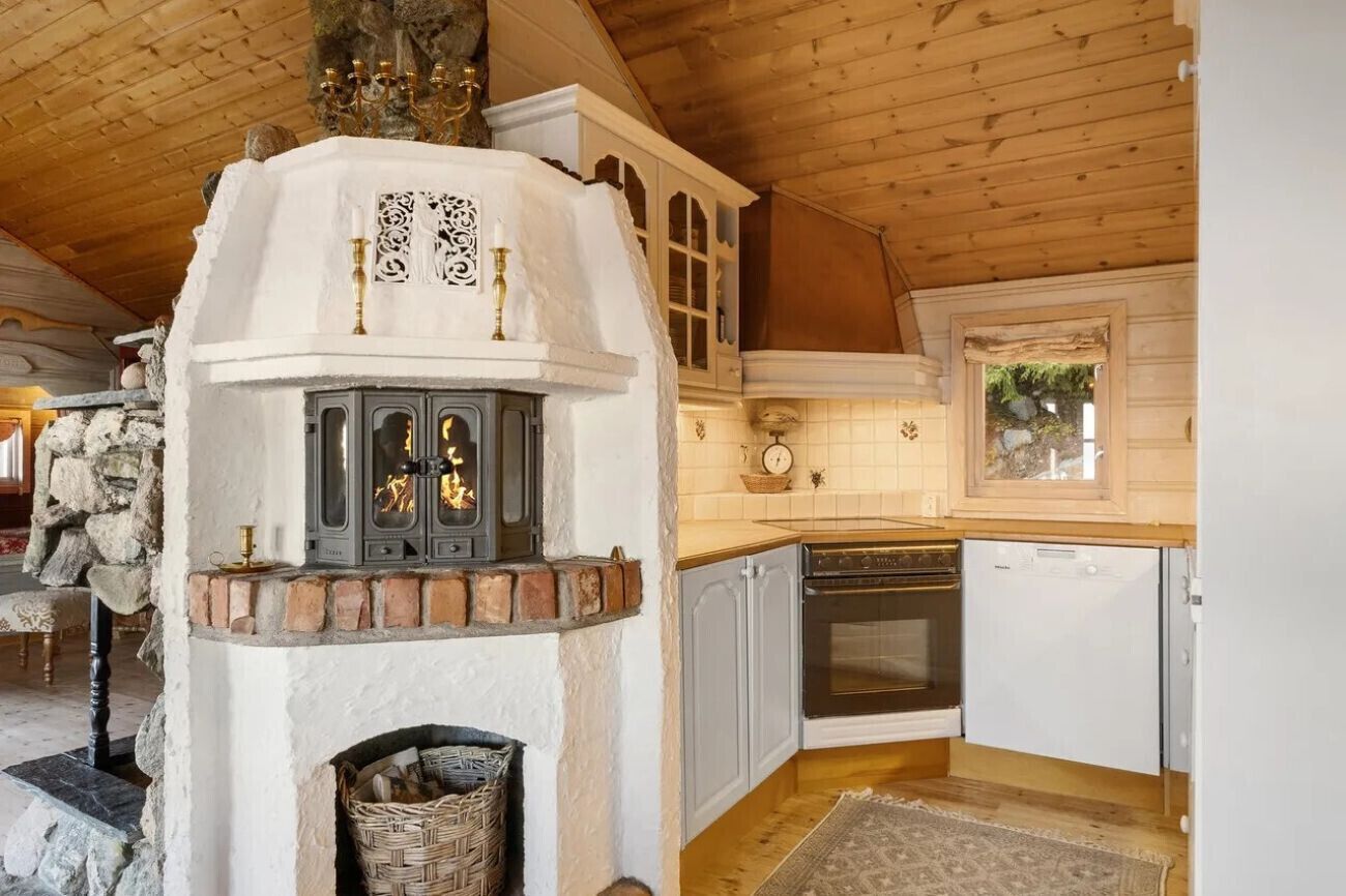 A rustic kitchen with a stone fireplace, wooden cabinets, and a small window.