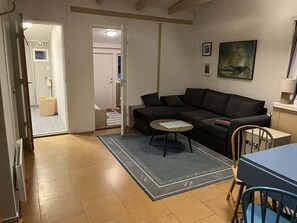 Uma sala de estar com sofá, uma mesinha redonda, uma poltrona azul, um abajur e um quadro na parede.