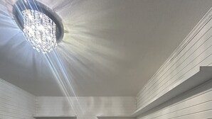 Une chambre à coucher moderne avec un lit, un miroir rond, un petit tabouret et un luminaire fixé au plafond.