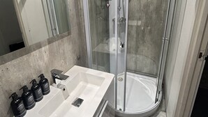 Une salle de bain moderne avec une douche en verre, un lavabo blanc doté de distributeurs de savon et un grand miroir.