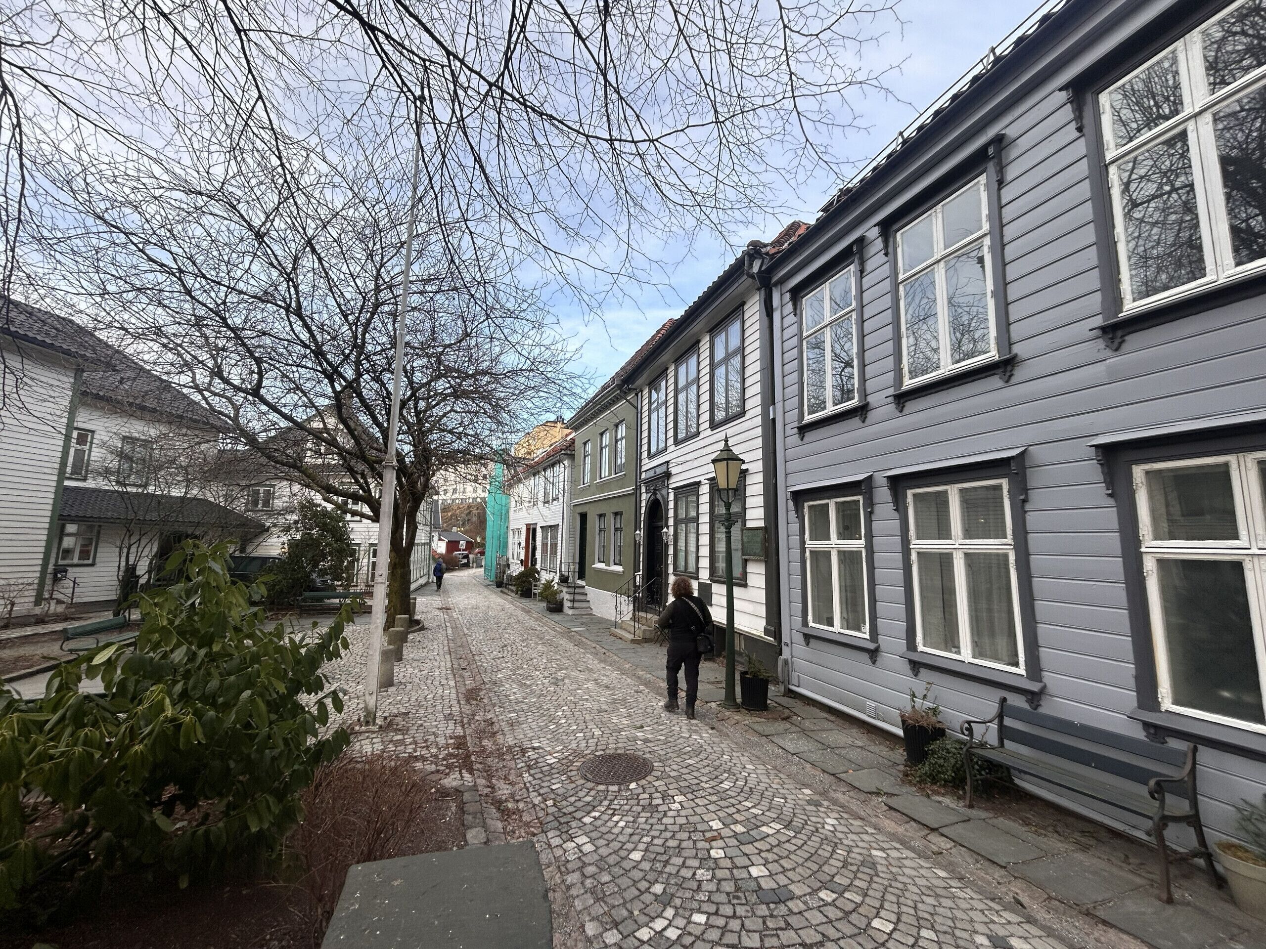 A cobblestone street lined with traditional buildings, a pedestrian, and a bench.