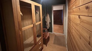 Un armario de madera con puertas de cristal, un banco, un perchero y una puerta que da a otra habitación.