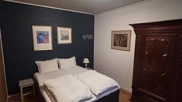 Een slaapkamer met een bed, een nachtkastje, een dressoir en lijstjes met kunstwerken aan de muur.