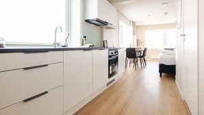 A modern kitchen with white cabinetry, a built-in oven, and a dining area with a table and chairs. - Lofoten Premium Suites #Aurora (Vestvågøy)