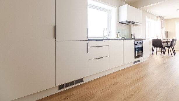 A modern kitchen with white cabinetry, a built-in oven, and a dining area with a table and chairs. - Lofoten Premium Suites #Aurora (Vestvågøy)