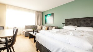 A hotel room with a bed, a sofa, a dining table, and a painting on the wall. - Lofoten Premium Suites #Aurora (Vestvågøy)