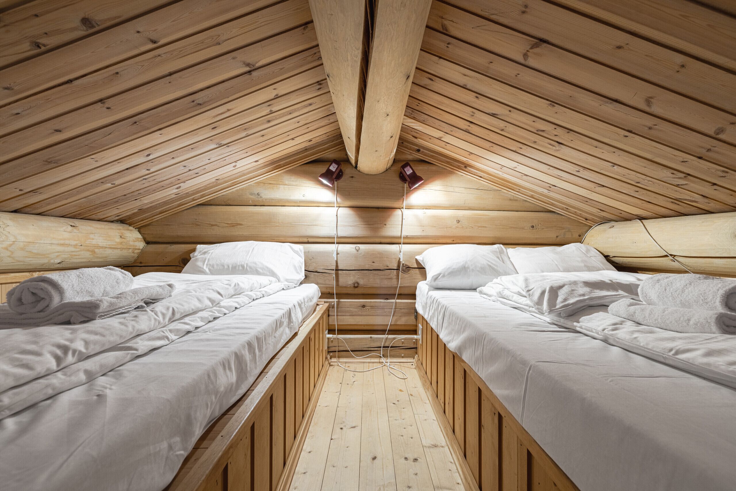 A small, wooden cabin with two beds, a sloped ceiling, and a simple, rustic interior.