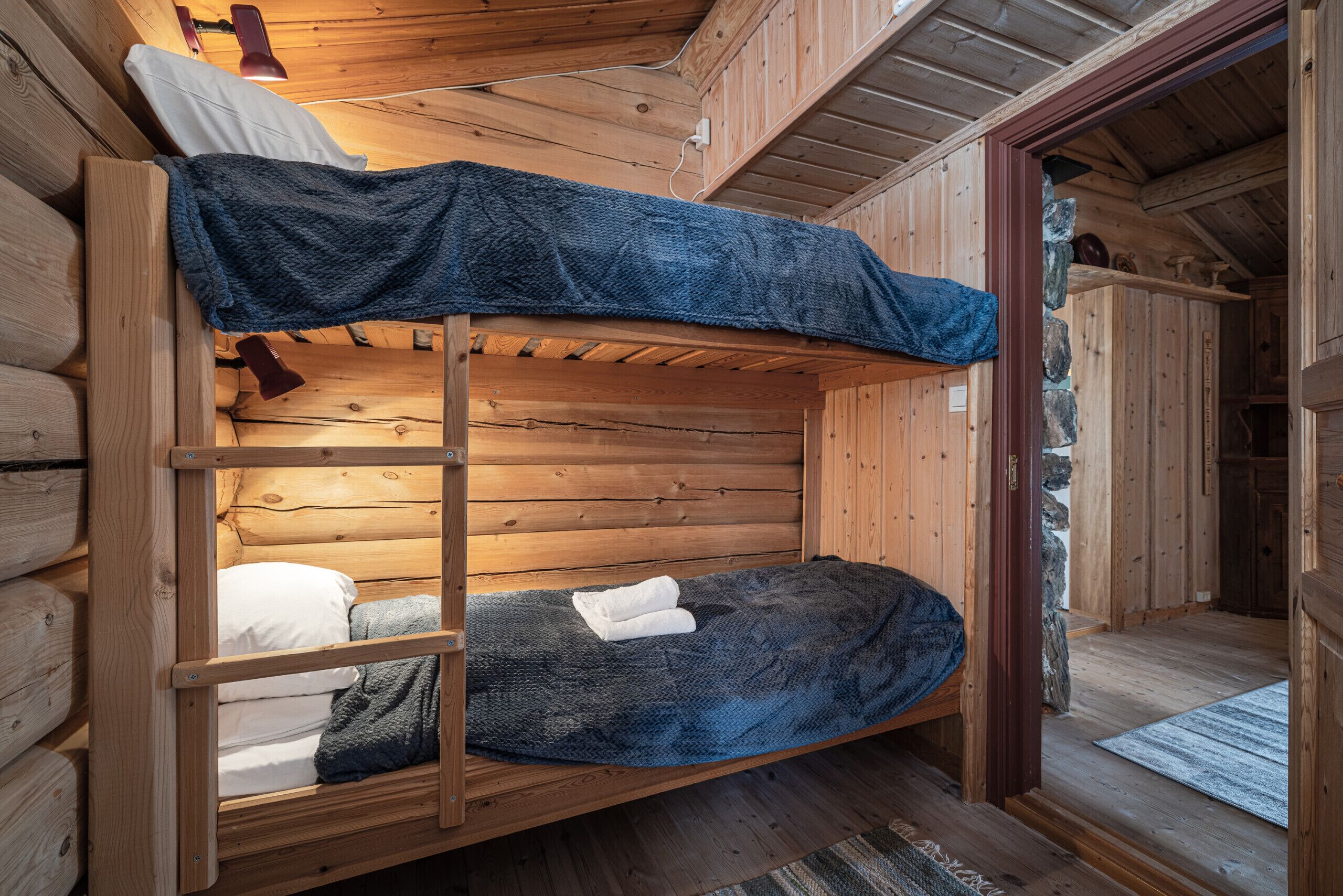 A bunk bed with a ladder, wooden walls, and a small window.