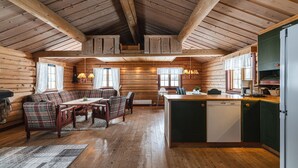 L’intérieur d’une cabane en rondins est doté d’un plafond en bois, d’un coin repas avec une table et des chaises, d’une cuisine équipée d’un lave-vaisselle et d’un canapé.