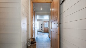 Un couloir étroit aux murs en bois, doté d’un sol carrelé en pierre et terminé par une porte en bois.