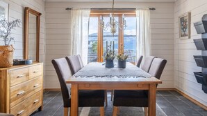 Une salle à manger avec une table en bois, des chaises, un lustre et une vue sur les montagnes, visible à travers de grandes fenêtres.