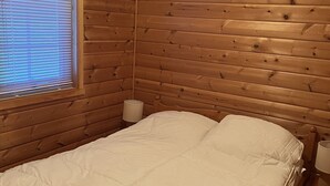 A wooden cabin bedroom with a bed, a window with blinds, and a nightstand with a lamp. - Pollstua, cosy cabin with amazing views (Vestvågøy)