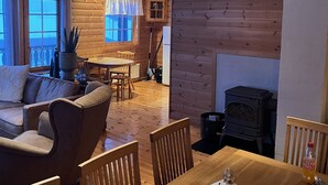 A cozy cabin interior with a wooden dining table, chairs, a sofa, a fireplace, and a kitchen area. - Pollstua, cosy cabin with amazing views (Vestvågøy)