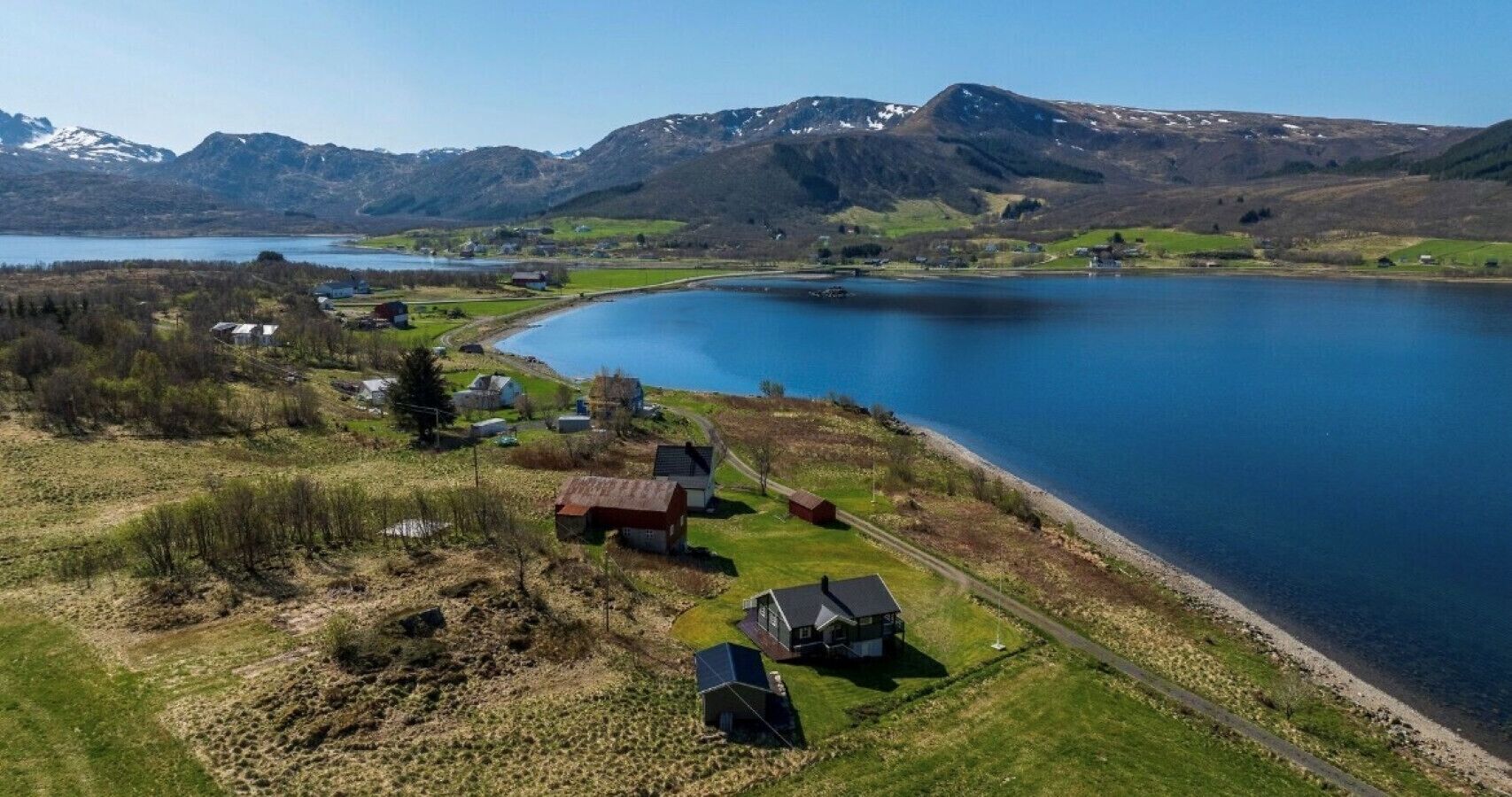 A lakeside property with a small cluster of houses, a dock, and a clear view of the surrounding mountains.