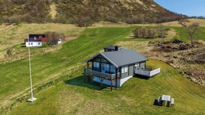 A two-story house with a balcony, surrounded by a grassy field and a hill in the background. - Pollstua, cosy cabin with amazing views (Vestvågøy)