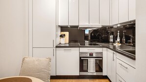 Eine kompakte Küche mit weißen Schränken, einer schwarzen Arbeitsplatte, einem eingebauten Backofen und einer Edelstahl-Dunstabzugshaube.