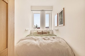 A bedroom with a bed, a window, and a plant.