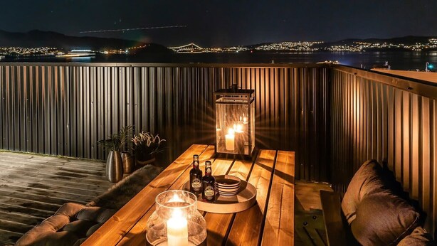 Eine Holzdar Terrasse mit einem Tisch für zwei Personen, ausgestattet mit einer Kerze, Flaschen und einem Glas.