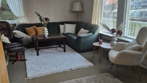 Una sala de estar con sofá, sillones, una mesa de centro, una lámpara y vistas a las montañas por la ventana.