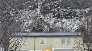 Un edificio de dos pisos con un garaje, un camino de entrada y montañas al fondo.