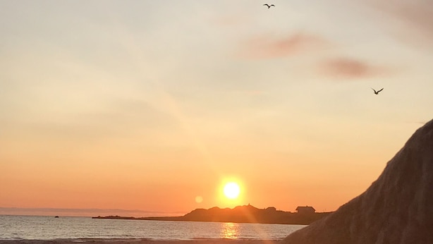 Un atardecer sobre una playa con una gran formación rocosa en primer plano.