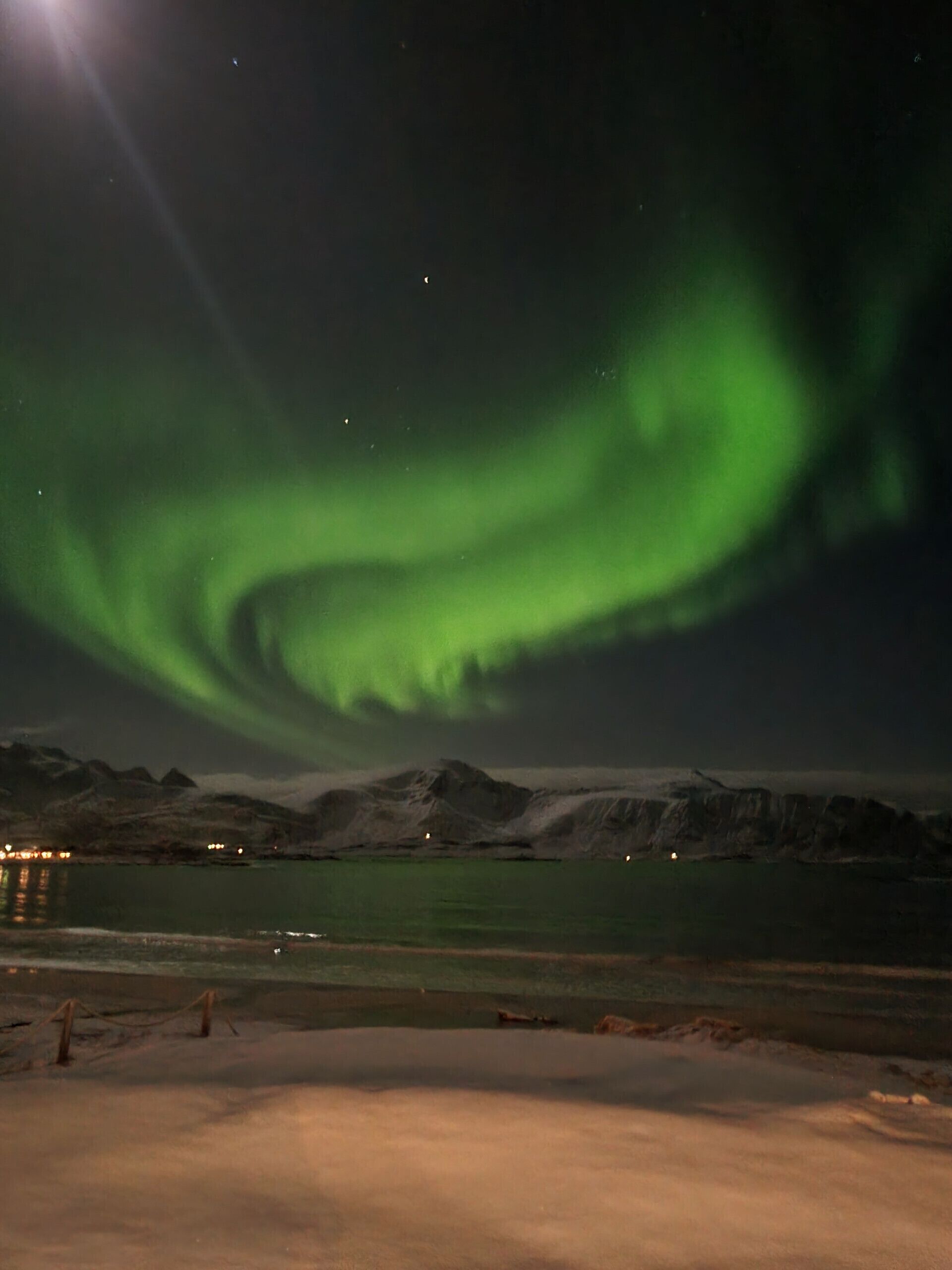 A night sky with the Northern Lights over a mountainous landscape.