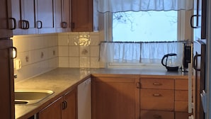 Una cocina compacta con armarios de madera, un lavamanos, una ventana con cortinas y una tetera sobre la encimera.