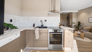 Cucina moderna con piano cottura, forno e lavello integrati, mobili in legno e schienale in marmo.