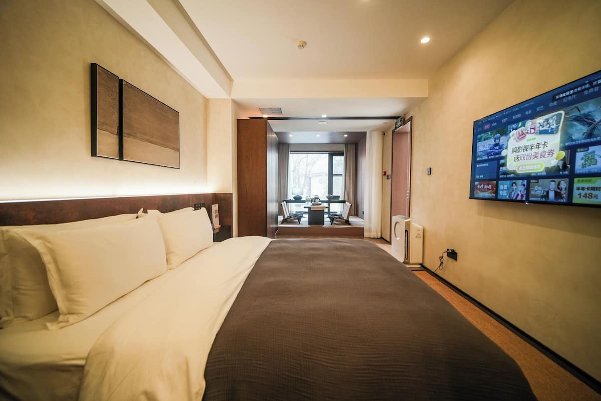 Une chambre d’hôtel avec un grand lit, un téléviseur fixé au mur et une vue sur la salle à manger.