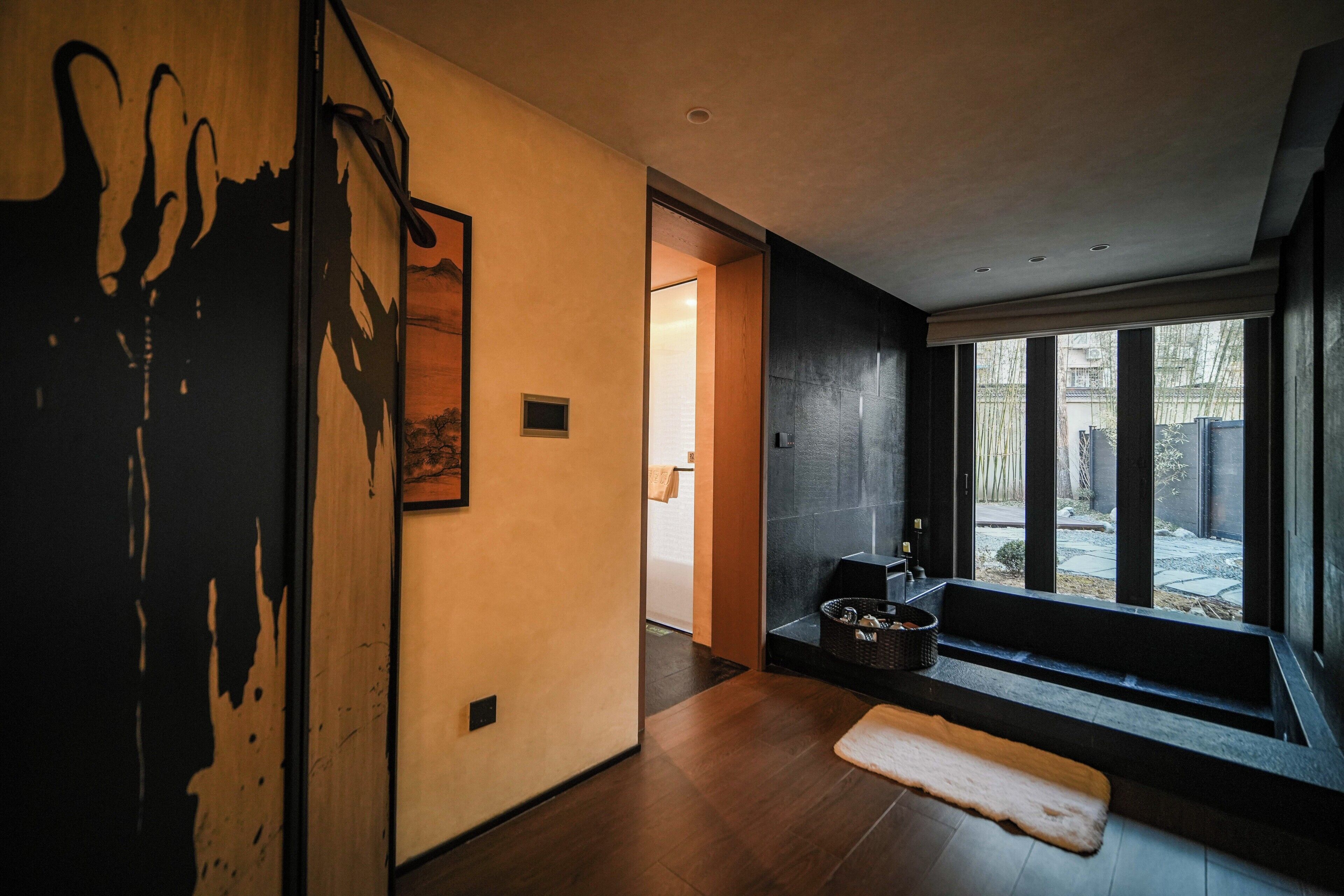 A modern interior with a wooden floor, a large window, and a door leading to another room.