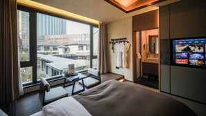 A modern hotel room with a large bed, a desk with a chair, a TV, and a view of the city.