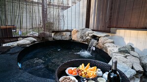 A hot tub surrounded by rocks and a basket of fruits and bottles.
