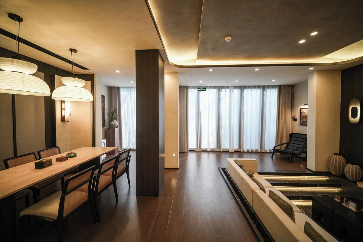 Un hall d’hôtel moderne avec un comptoir d’accueil en bois, un espace salon et de grandes fenêtres dotées de rideaux.