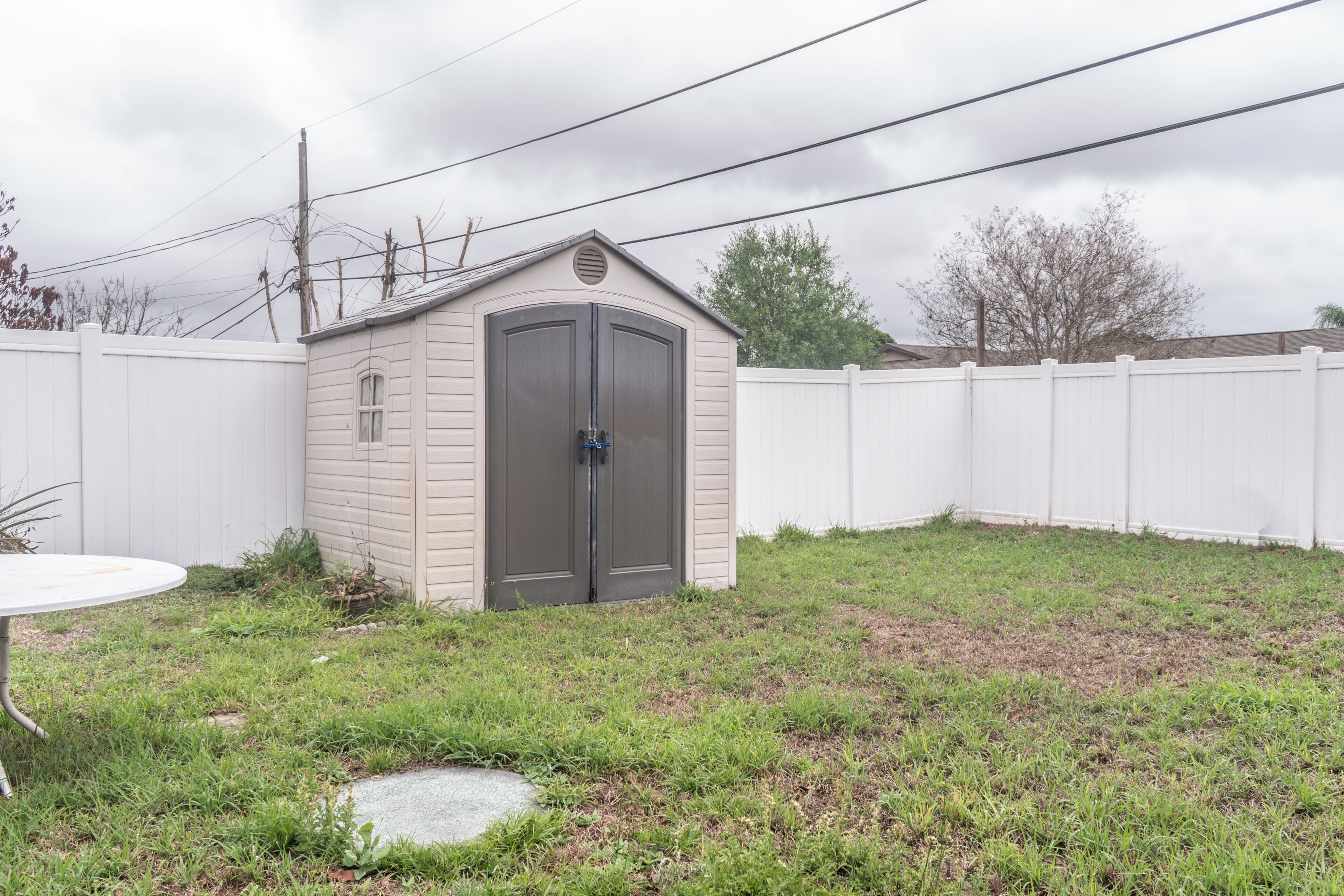 A small shed with a door and windows, surrounded by a white fence and grass.