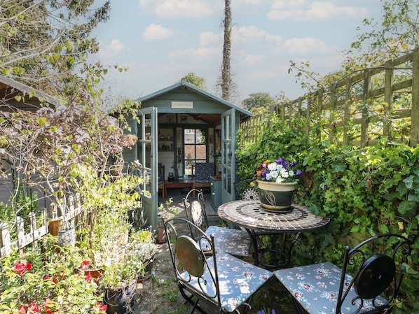 A garden with a gazebo, a round table with chairs, and potted plants.
