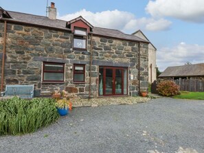 A stone building with a gravel driveway, a wooden bench, and a small garden area. - Hafod, Ty Mawr Farm in Llanddeiniolen (Caernarfon)