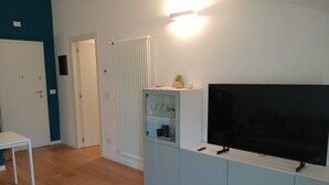 A modern living room with a flat-screen TV, a glass cabinet with decorative items, and a white door. - COMFY & COZY, in the heart of Chiavari, cozy two-room special and perfect" (Chiavari)