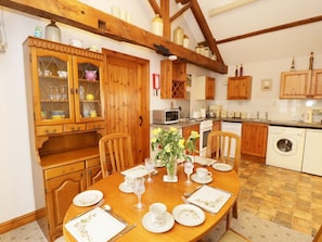 A dining area with a wooden table set for four, surrounded by wooden cabinets and a kitchen in the background.