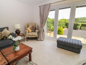 Ein Wohnzimmer mit Sofa, Sessel, Hocker und Couchtisch mit Blumen in einer Vase.