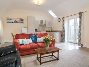 A living room with a red sofa, a coffee table, and a kitchen in the background. - Millstone Cottages - Middle Cottage, Westbury (Shrewsbury)