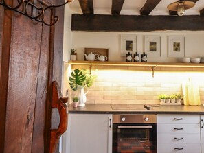 Une cuisine avec une porte en bois, un poêle, un plan de travail orné de plantes en pot et des tableaux encadrés accrochés au mur.