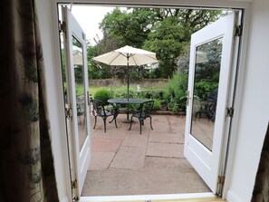 Puerta abierta a un patio exterior con una mesa, sillas, una sombrilla y vistas a un jardín.