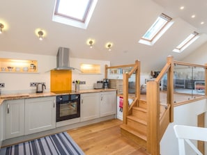 A modern kitchen with a built-in oven, a gas stove, and a stainless steel range hood. There is a wooden staircase leading to an upper level. - Bishop's Castle Barn, Bishop's Castle (Bishop's Castle)