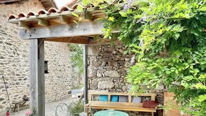 Un mur de pierres, une pergola en bois, un espace salon extérieur et une terrasse en gravier.