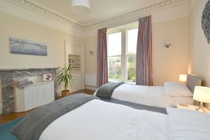 A hotel room with two beds, a fireplace, a bookshelf, and a view of greenery.
